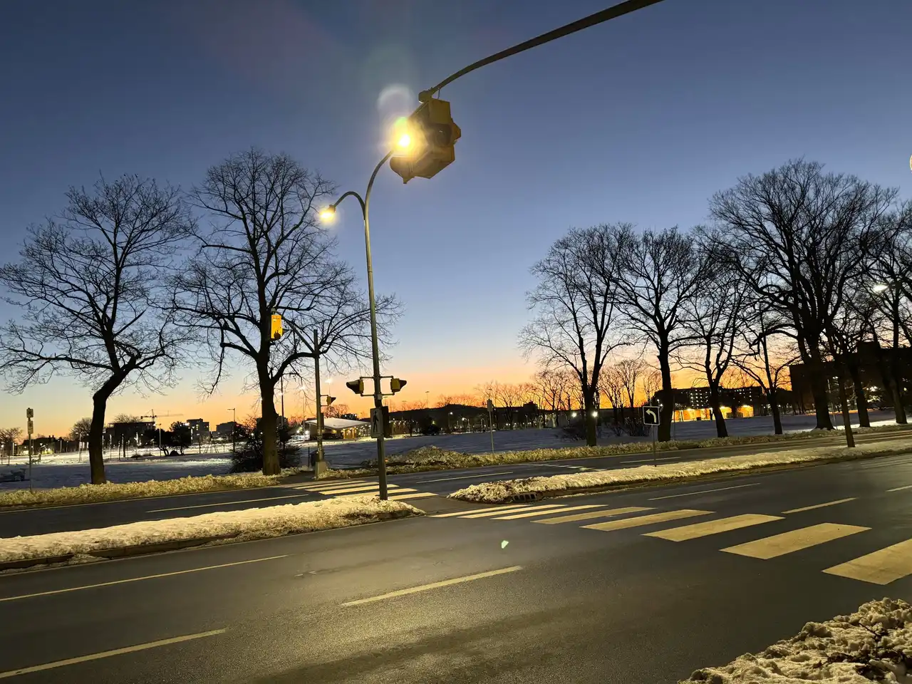 An empty city crossing at dusk, a street light on against a blue and orange sky