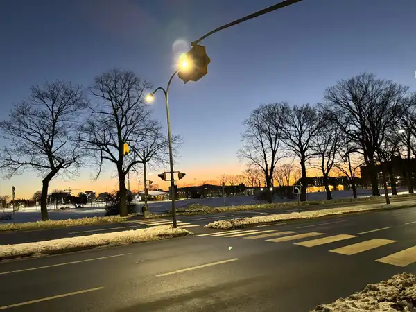 An empty city crossing at dusk, a street light on against a blue and orange sky