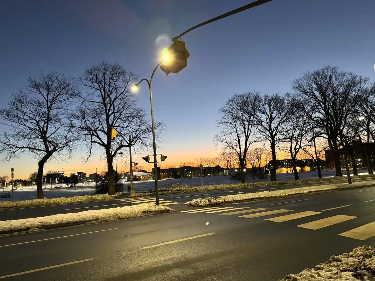 An empty city crossing at dusk, a street light on against a blue and orange sky