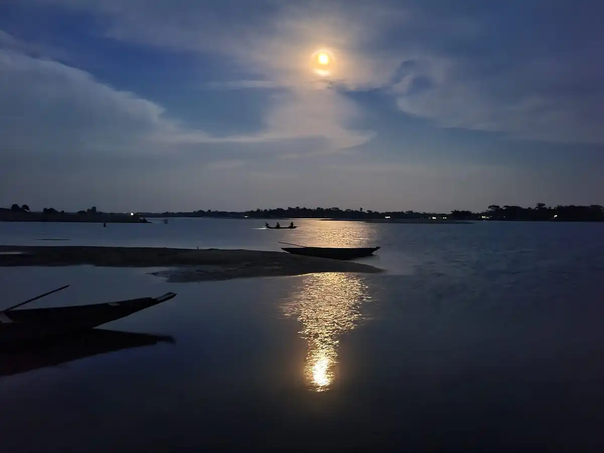 Moonlight reflected on a calm river with two wooden boats moored near the shore